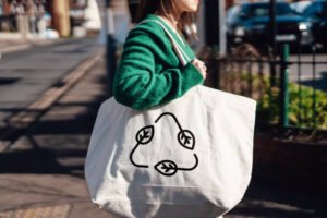Midsection of young woman carrying reusable shopping with a recycling symbol. Environment protection, ethical consumerism and recycling concept.