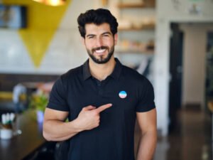 A young man standing in a cafe, with an I VOTED sticker on his shirt.