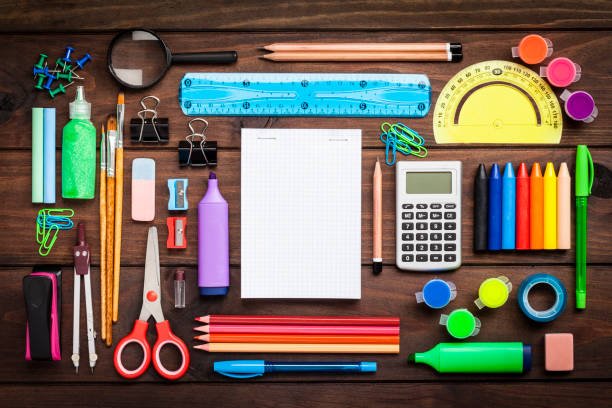Top view of a large group of multi colored school or office supplies shot on rustic dark wooden table. A blank note pad is at the center of the composition with useful copy space ready for text and/or logo. DSRL studio photo taken with Canon EOS 5D Mk II and Canon EF 100mm f/2.8L Macro IS USM
